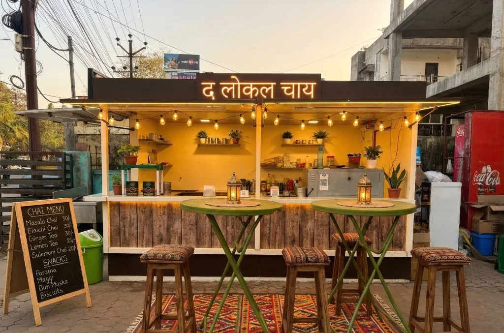 The Local Chai outdoor seating at dusk - yellow counter, fairy lights, and the neon द लोकल चाय sign